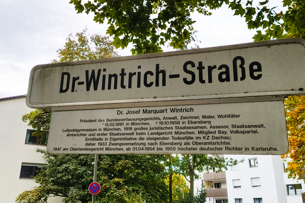 Straßenschild mit der Aufschrift "Dr-Wintrich-Straße", darunter ein Legendenschild mit der Beschriftung "Dr. Josef Marquart Wintrich Präsident des Bundesverfassungsgerichts, Anwalt, Zeichner, Maler, Wohltäter *15.02.1891 in München, †19.10.1958 in Ebersberg Luitpoldgymnasium in München, 1918 großes juristisches Staatsexamen. Assessor, Staatsanwalt, Amtsrichter und erster Staatsanwalt beim Landgericht München. Mitglied Bay. Volkspartei. Ermittelte in Eigeninitiative die steigenden Todesfälle im KZ Dachau; daher 1933 Zwangsversetzung nach Ebersberg als Oberamtsrichter. 1947 am Oberlandesgericht München, ab 01.04.1954 bis 1958 höchster deutscher Richter in Karlsruhe."