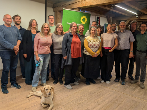 Die gewählten Grünen Listenkandidat:innen stehen nebeneinander vor einem Grünen Rollup. Im Vordergrund eine Hündin.
