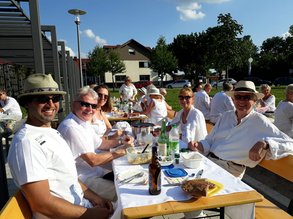 in weiß gekleidete Menschen sitzen an Biertisch