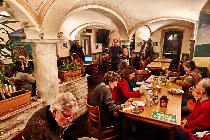 Raum mit Gewölbe, Interessierte sitzen an den Tischen und machen Notizen bzw. Essen. Der Referent Marc Block steht vor dem Publikum.